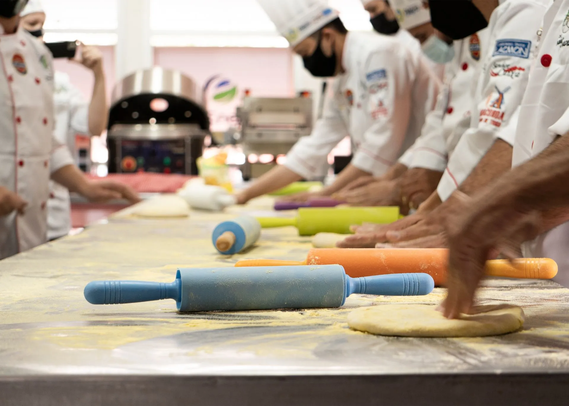 A chef guiding guests rolling fresh pasta dough at a long wooden table in a Florence cooking school