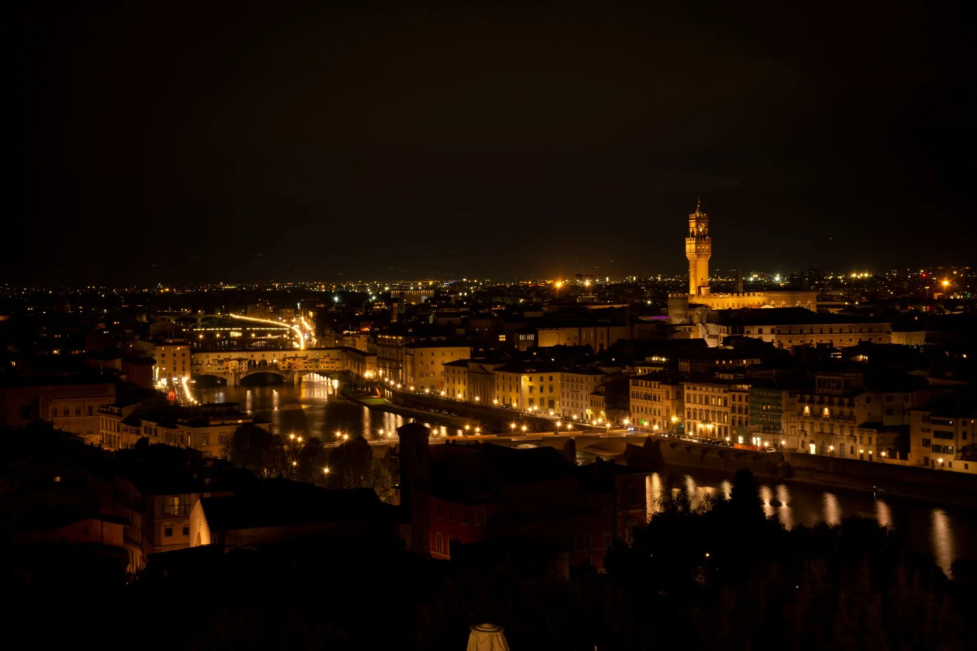 A narrow Florentine alley lit by a single lamp at night with the Duomo silhouetted beyond