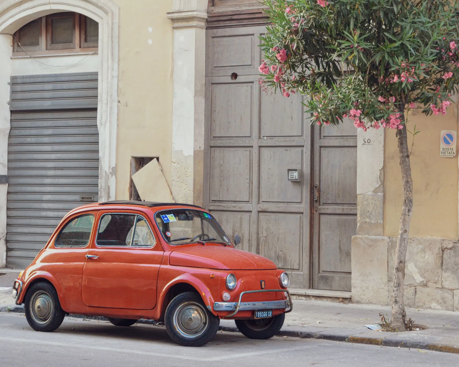 A line of pastel vintage Fiat 500 cars parked on a cypress-lined ridge above the Tuscan hills
