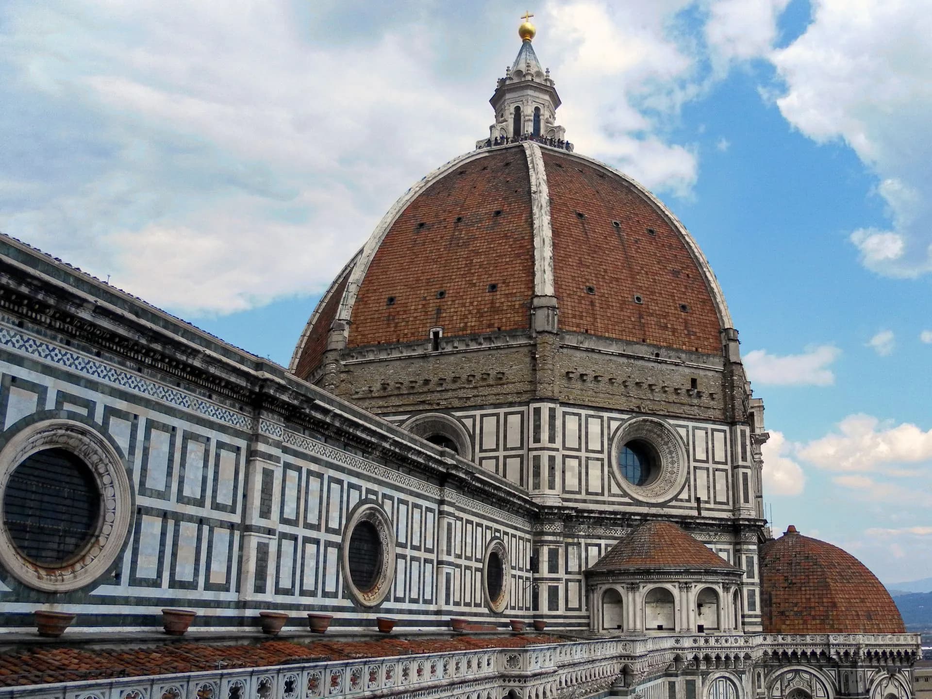 Brunelleschi's red-tiled dome and Giotto's marble bell tower rising above the rooftops of Florence at golden hour