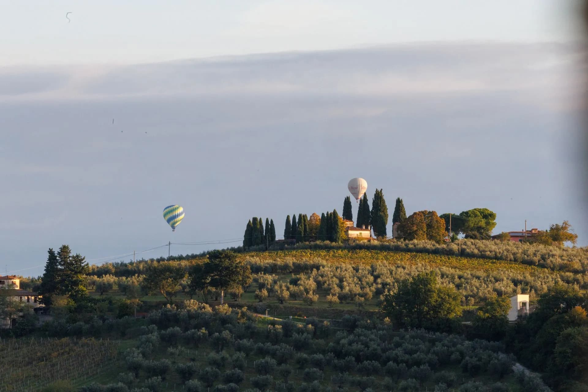 A hot air balloon drifting over mist-filled Chianti vineyards and cypress ridges at sunrise in Tuscany