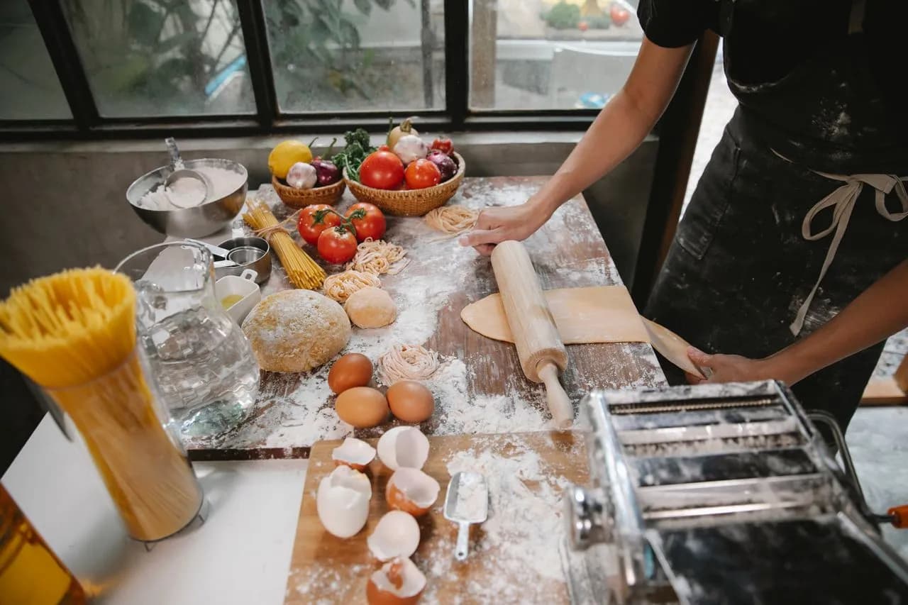 Hands rolling and cutting fresh tagliatelle on a floured wooden board at a Florence cooking class