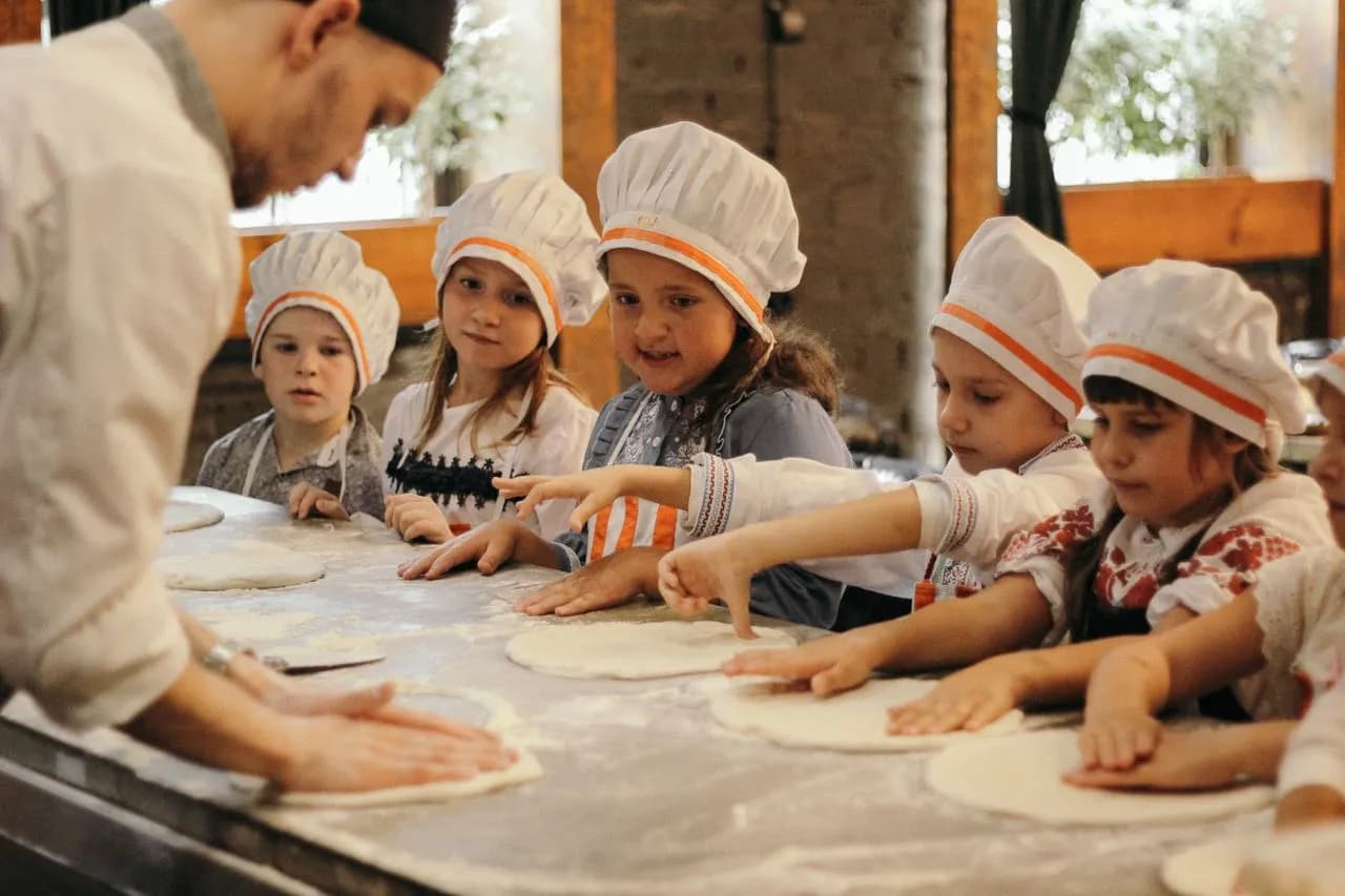 A hand stretching pizza dough beside a tub of freshly churned gelato at a Florence cooking class